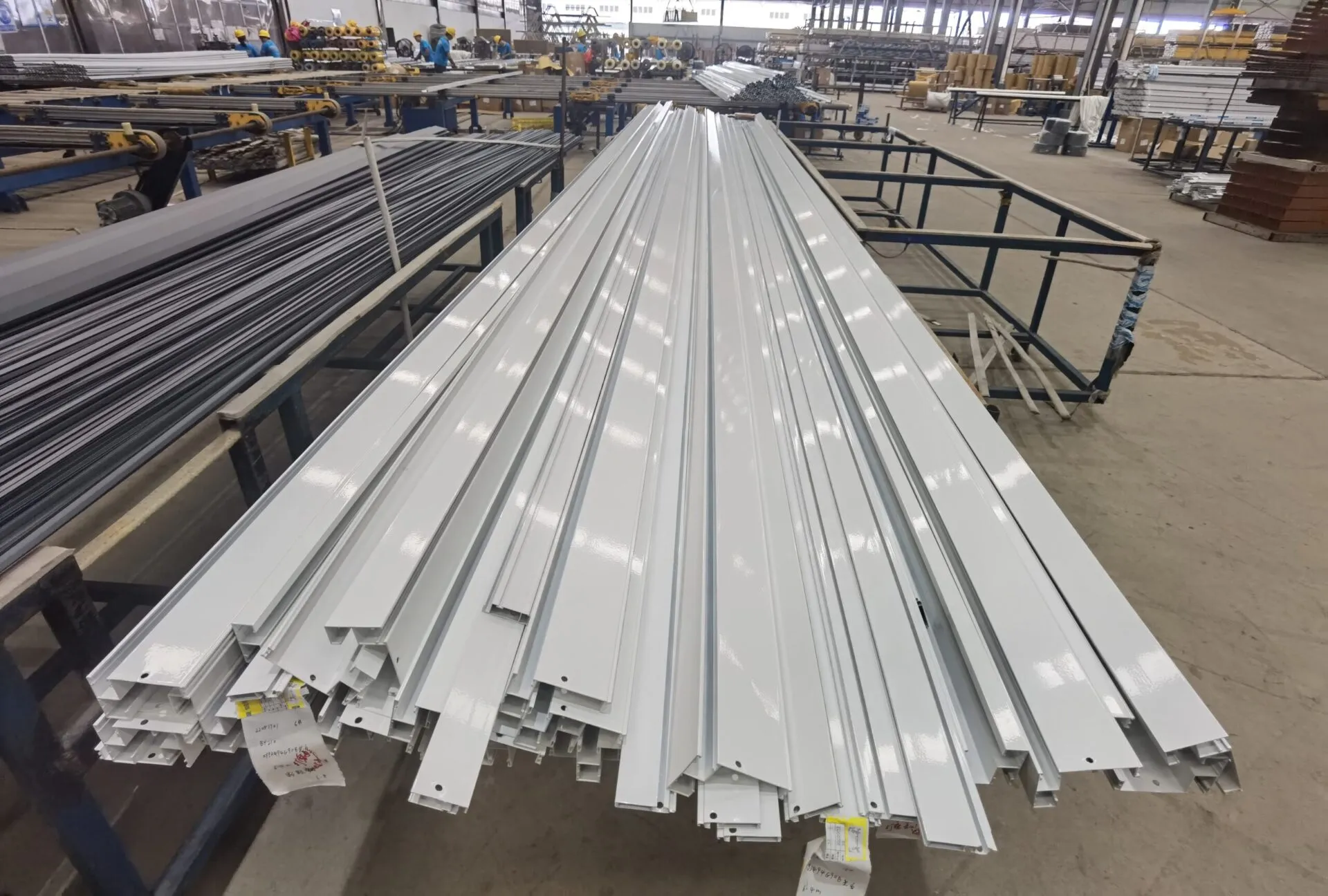 White powder-coated aluminium profiles laid out on a factory floor with paper labels